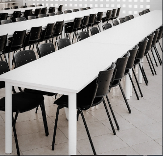 Mesas brancas compridas com cadeiras pretas em ambiente de refeitório